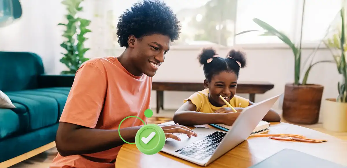 رجل وفتاة صغيرة يبتسمان أثناء استخدامهما جهاز كمبيوتر محمول معًا على طاولة.